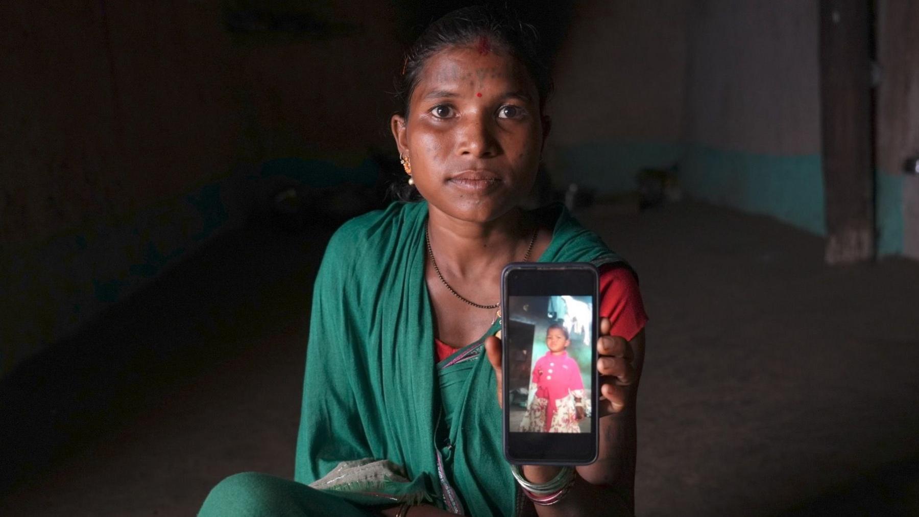 Woman in green saree holding smartphone with photograph of her daughter