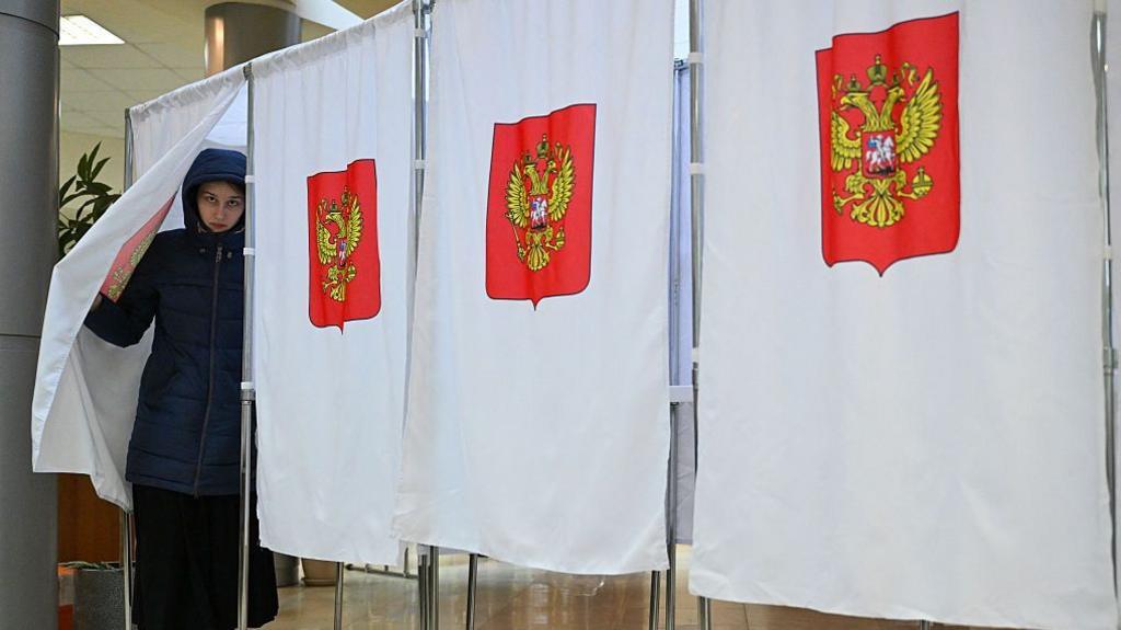 Woman in a blue parka steps out of a polling booth in Russia