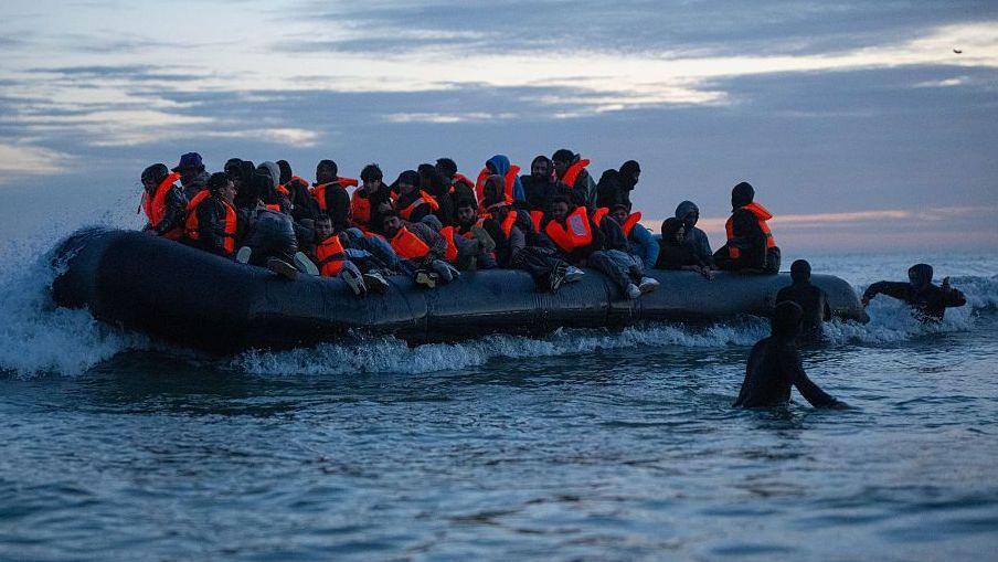 Men in orange life vests on a dinghy, ready to cross the Channel