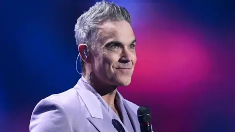Robbie Williams Reflects on British Self-Doubt as He Celebrates New Album Release