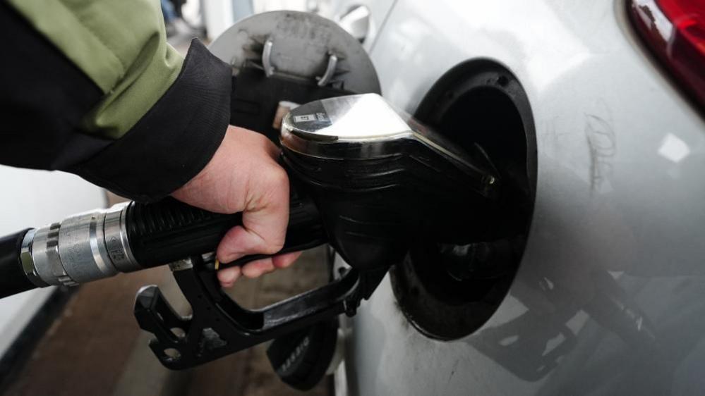 A diesel fuel pump is inserted into a grey car at a petrol station