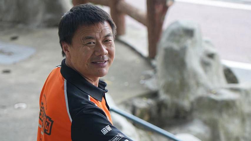 Wang Jibing in an orange polo smiling at the camera