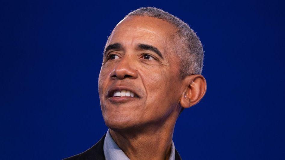 Barack Obama standing on a stage and smiling