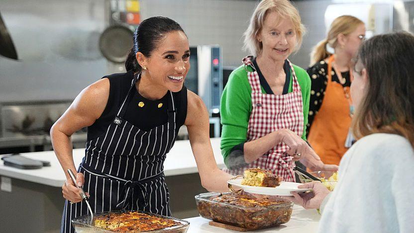 Meghan Markle smiles while she serves lunch to a woman