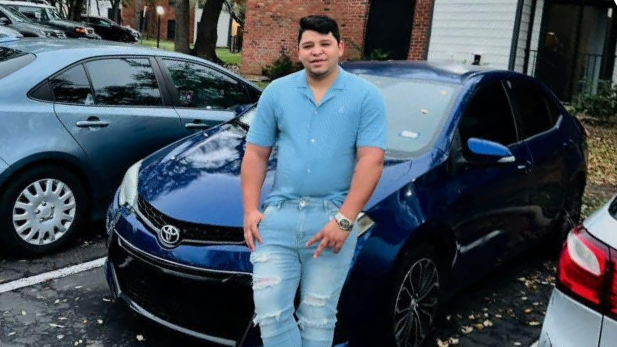 Wilber Rafael Garcés Perez leaning against a blue Honda, smiling