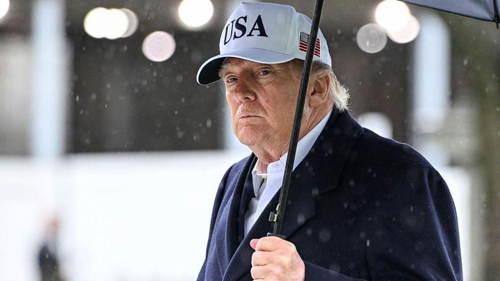 President Trump holds an umbrella as rain falls around him